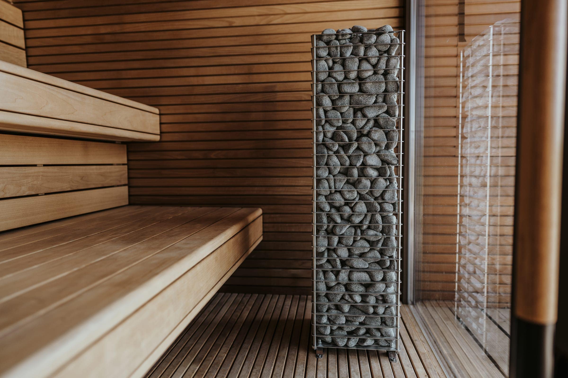 Tall stone-filled steel column of a HUUM CLIFF heater beside the bench of a thermowood sauna