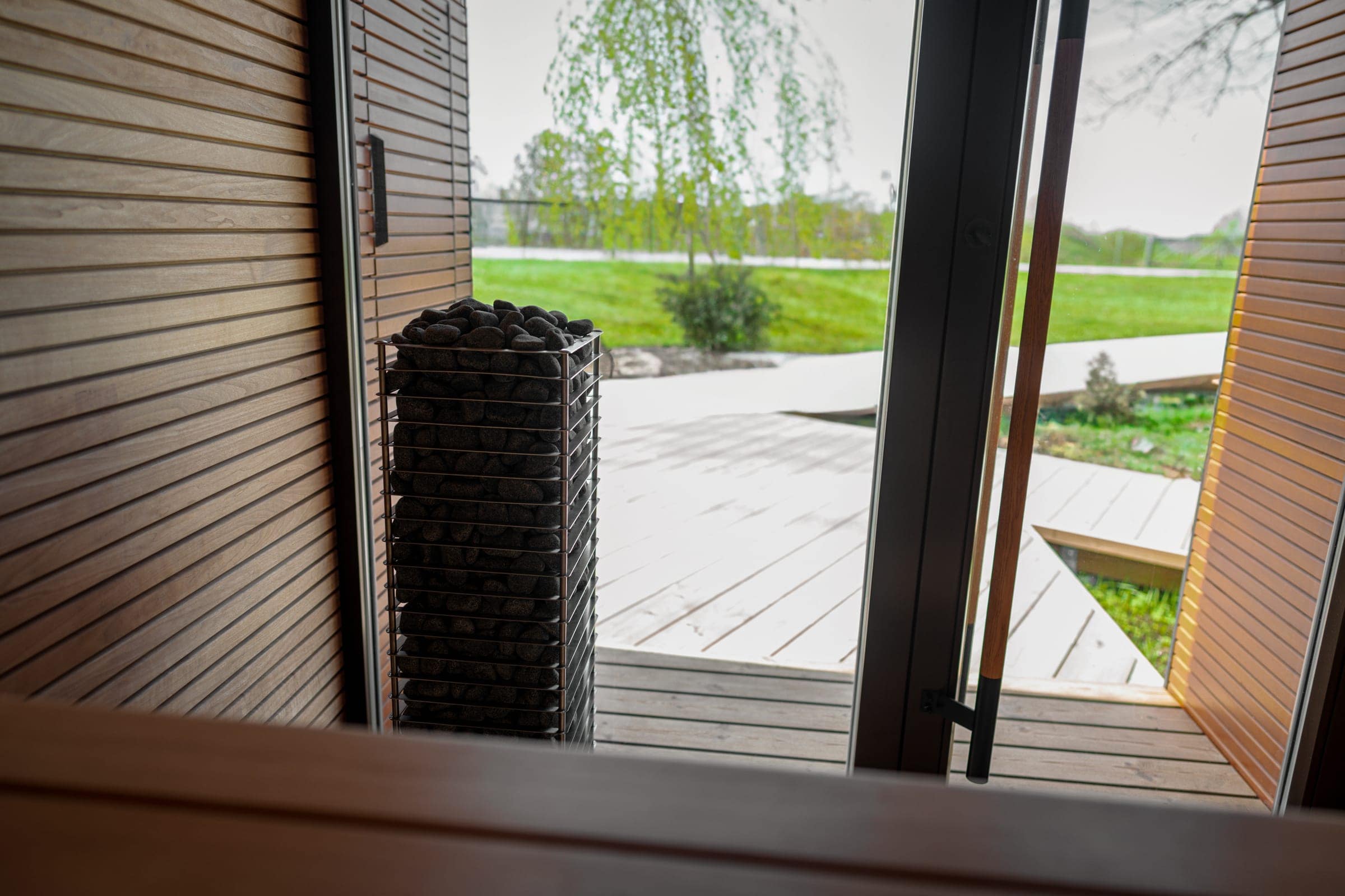 HUUM CLIFF standing beside a glass sauna door that opens onto a garden with birch trees