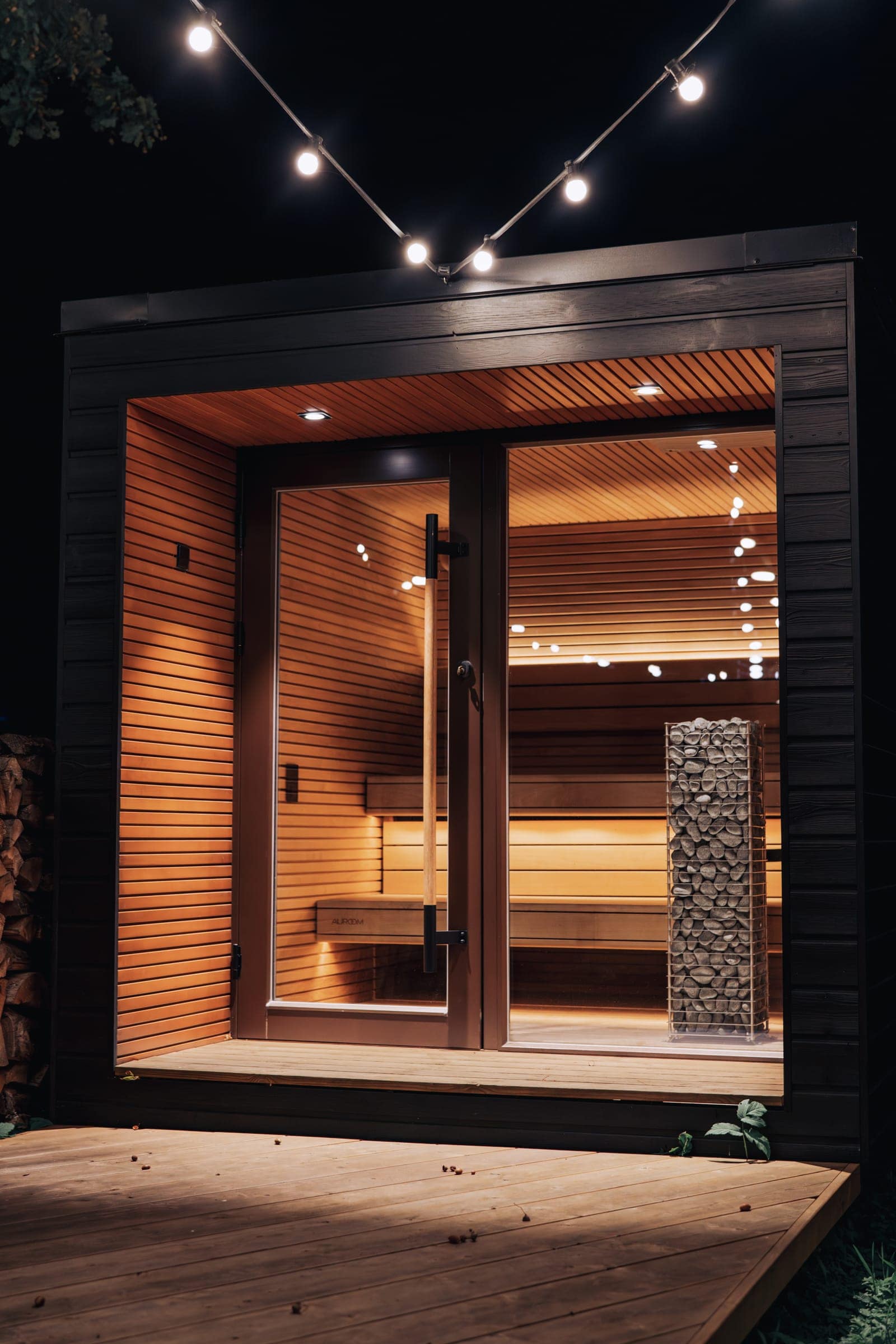 A glass-fronted sauna cabin at night with the HUUM CLIFF visible inside under warm light