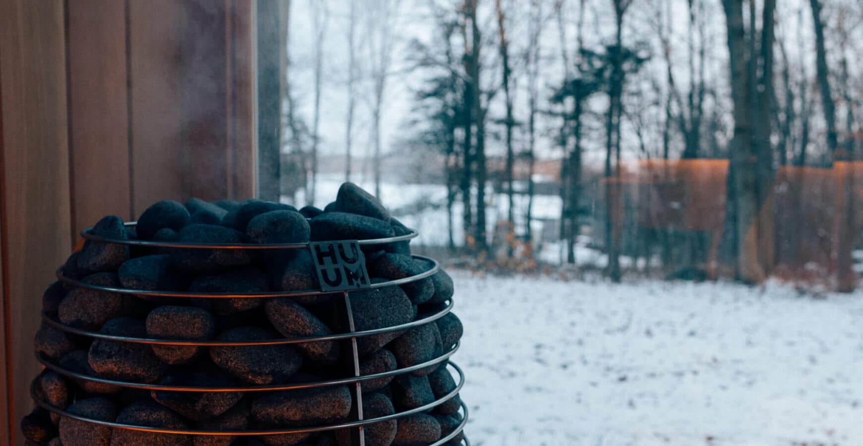 HUUM HIVE filled with dark stones in front of a window looking onto snowy woods