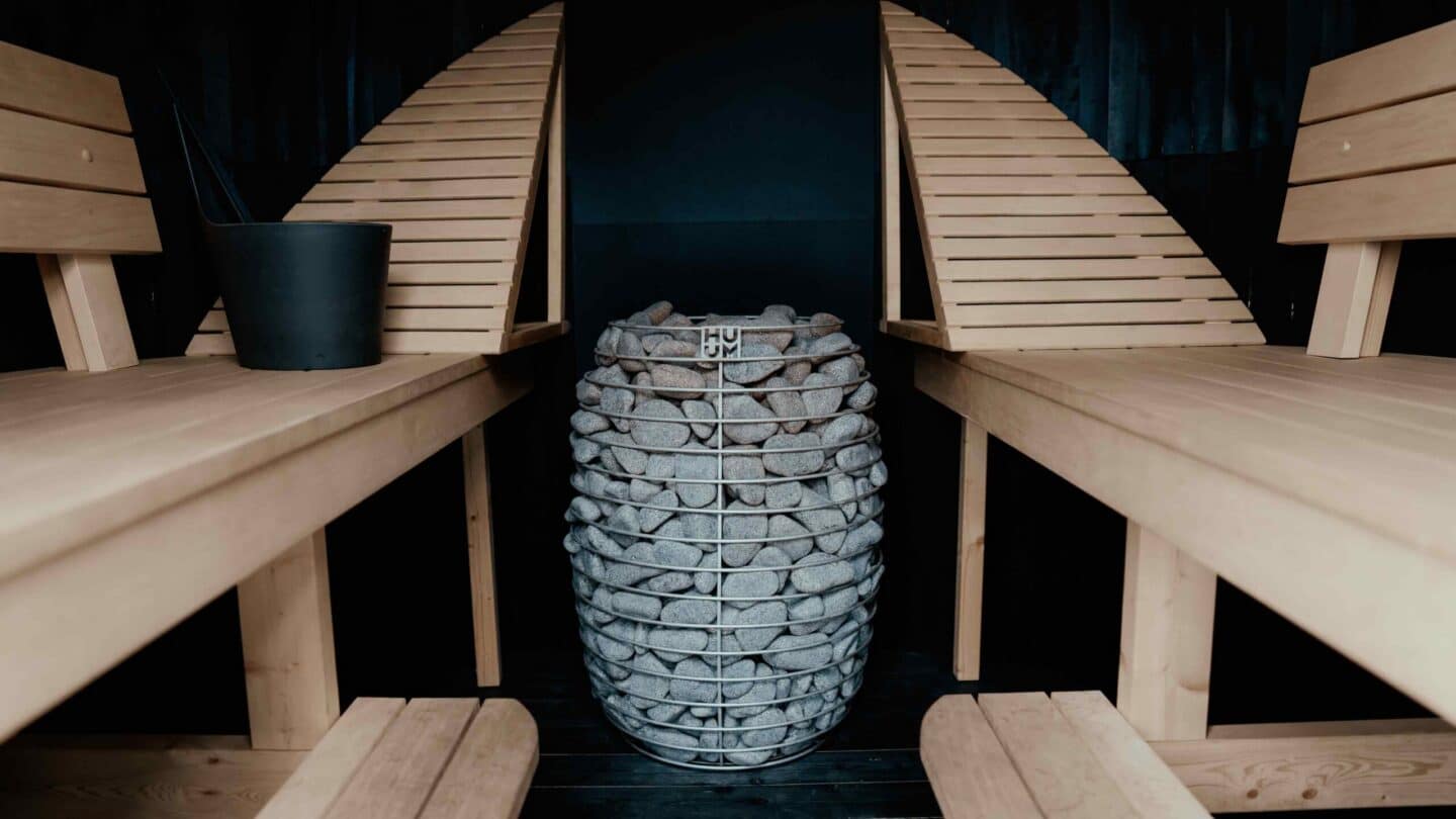 HUUM HIVE between two pale wood benches with slanted backrests in a dark sauna