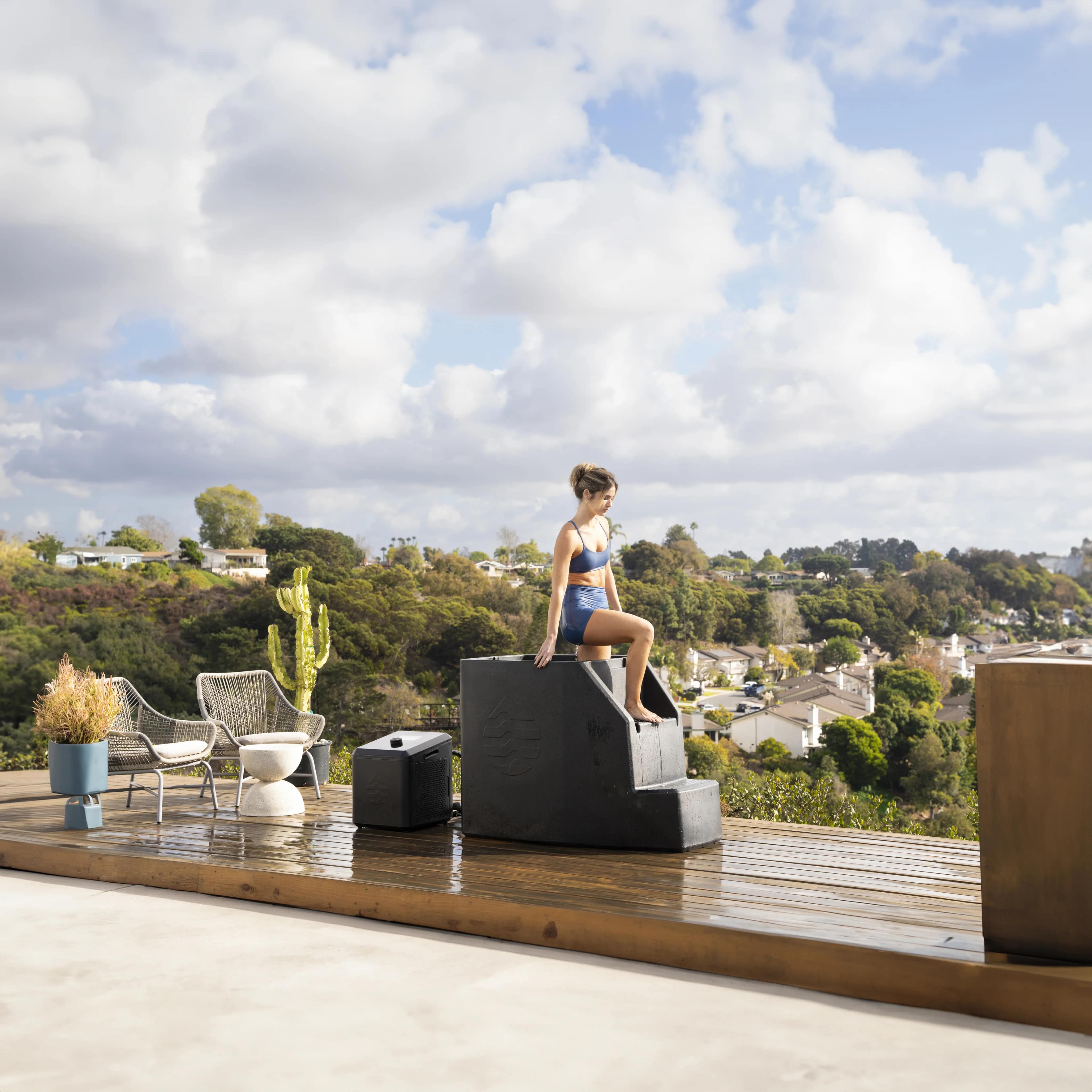 A woman sitting on the built-in steps of an Ice Barrel 500 on a rooftop deck beside a cactus