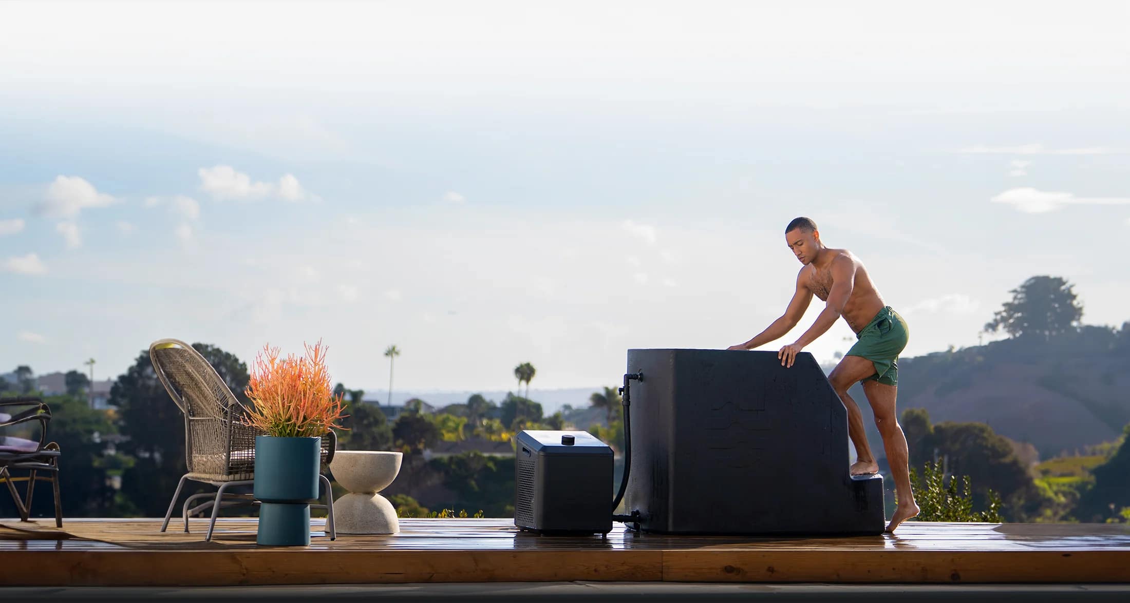 A man climbing onto an Ice Barrel 500 beside its chiller on a wooden deck overlooking hills