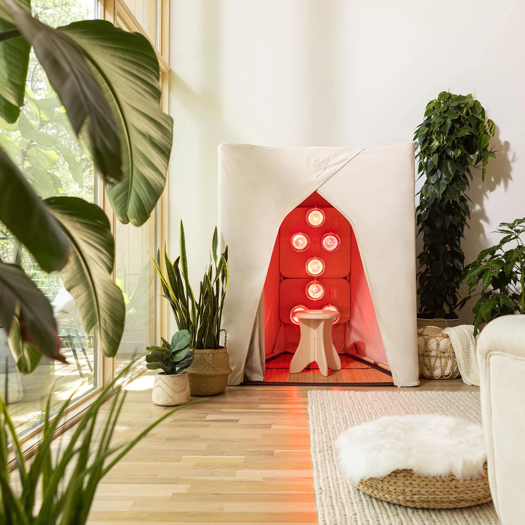 SaunaSpace FireLight canvas enclosure glowing red inside a bright room full of plants