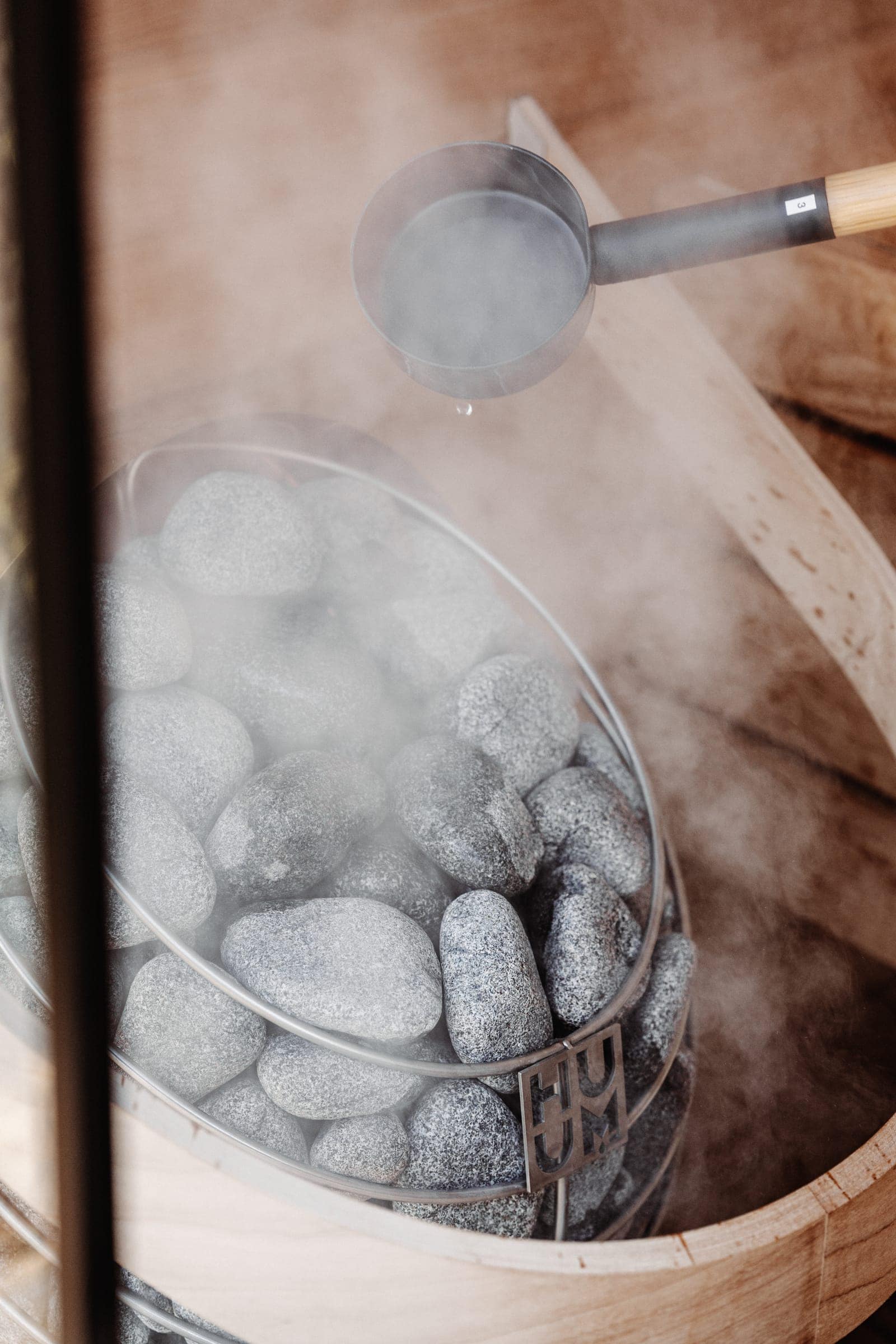 Water poured from a ladle sends steam up from the stones of a HUUM DROP heater