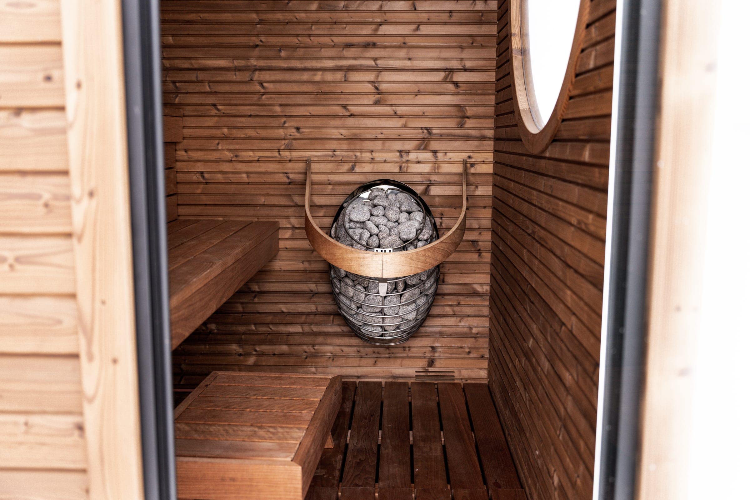 HUUM DROP with a curved wooden guard in the corner of a thermowood sauna with a round window