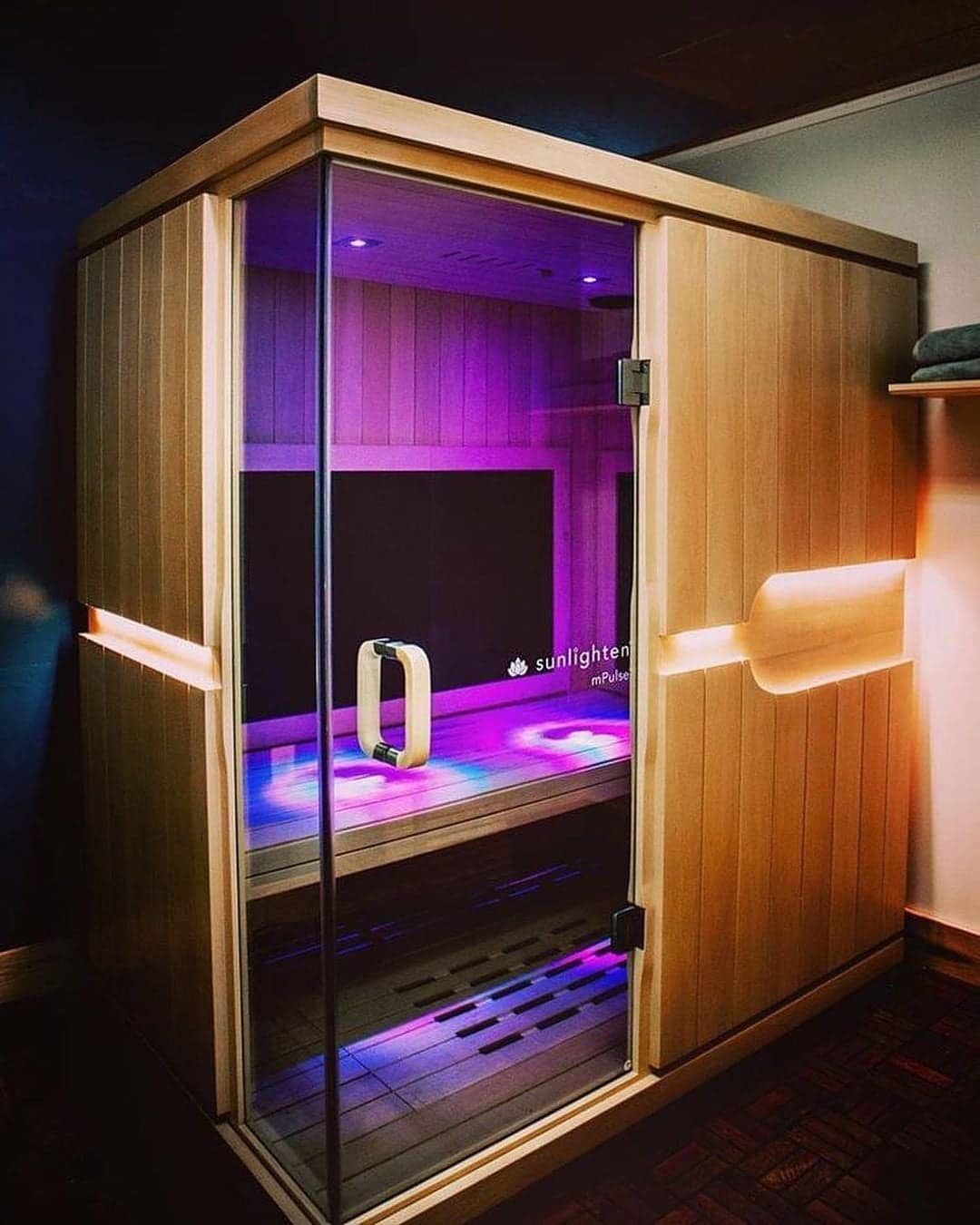 Sunlighten mPulse Conquer with a glass front and a purple-lit interior in a dim room