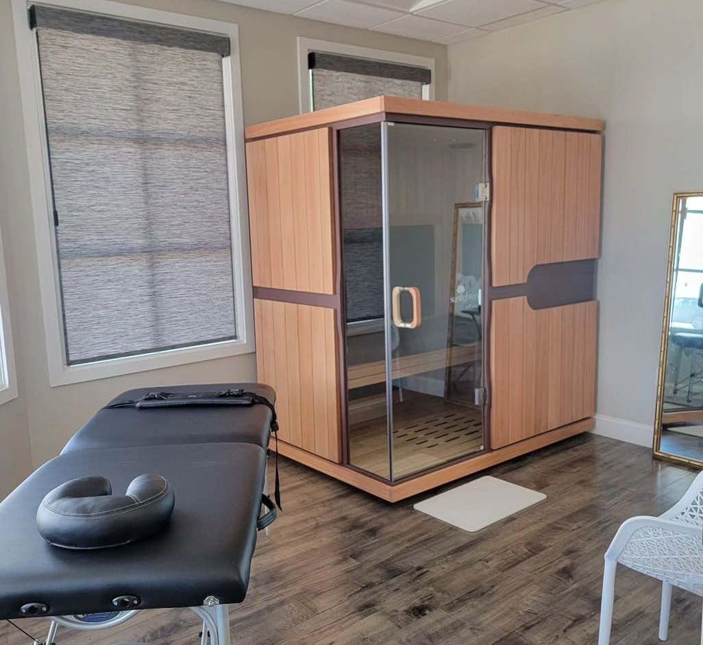 Sunlighten mPulse Conquer in a treatment room beside a massage table