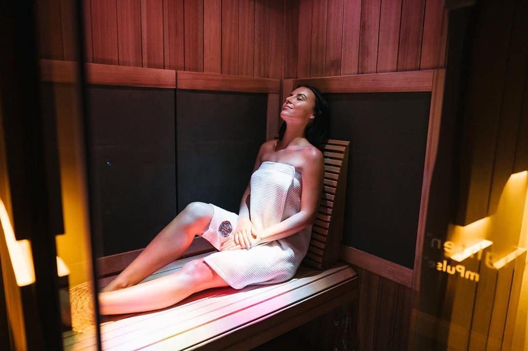 A woman in a towel reclining on the bench inside a Sunlighten mPulse under warm light