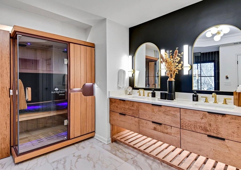 Sunlighten mPulse Believe with a cedar frame and glass front beside a double vanity in a marble bathroom