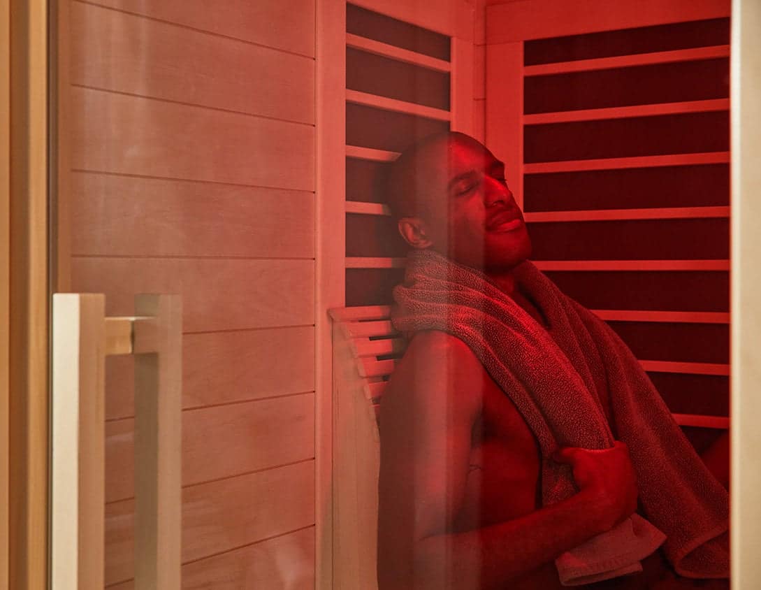 A man with a towel around his neck relaxing in a Sunlighten Signature under red light
