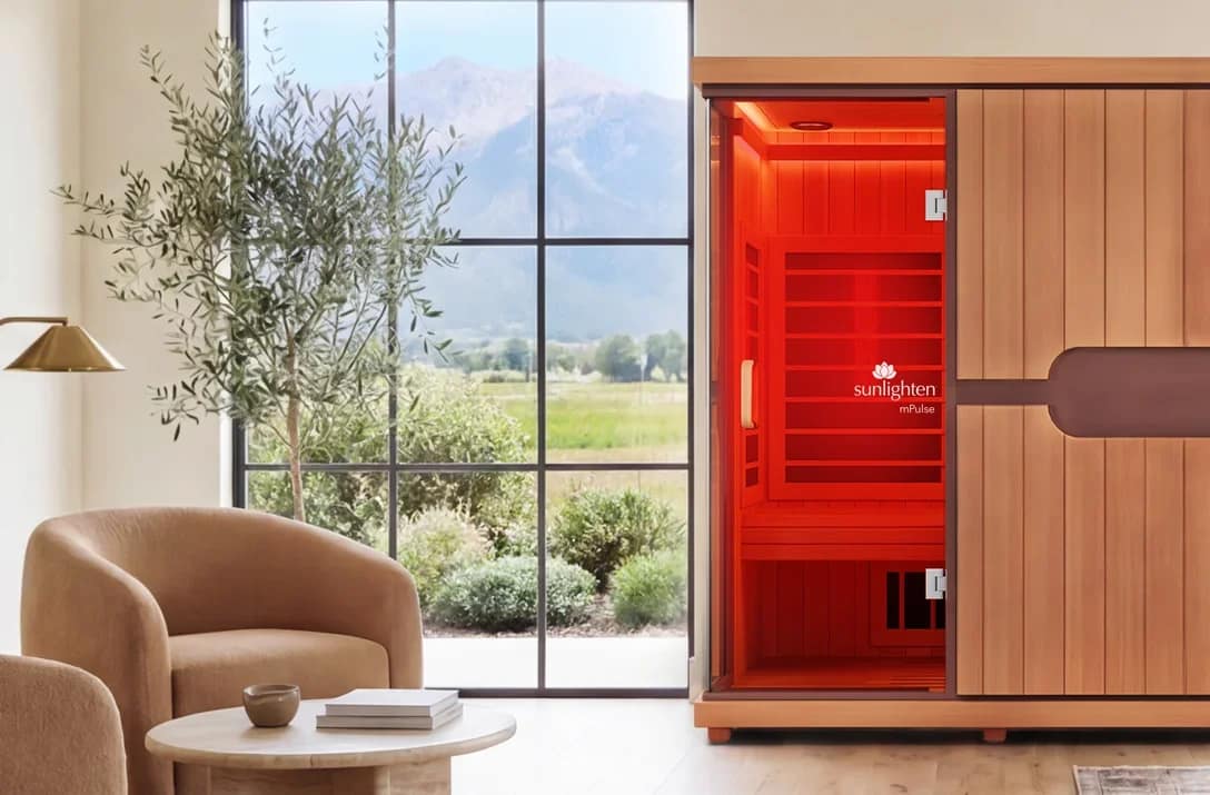 A Sunlighten mPulse Conquer stands in a bright living room with its door open and the cabin lit red.