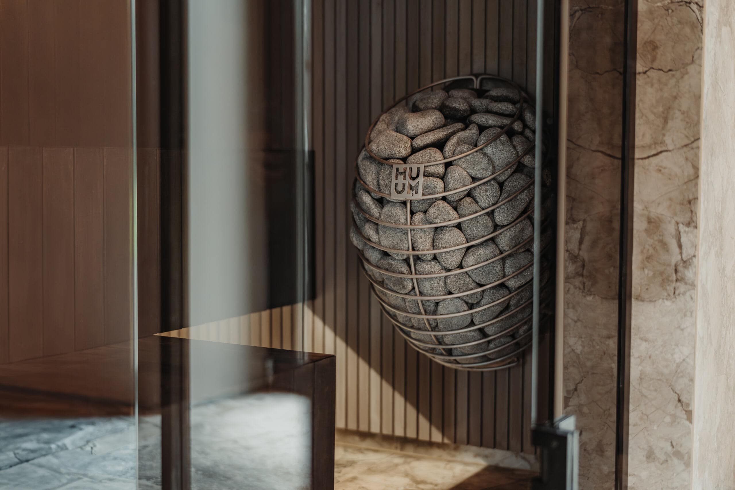 HUUM DROP heater on a slatted dark wall beside marble behind a glass sauna door