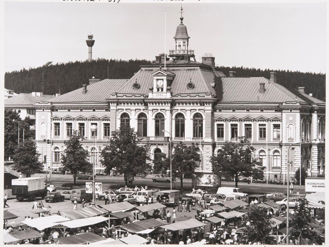 Market stalls fill the square in front of Kuopio's city hall in 1982, and Puijo tower stands on the wooded hill behind